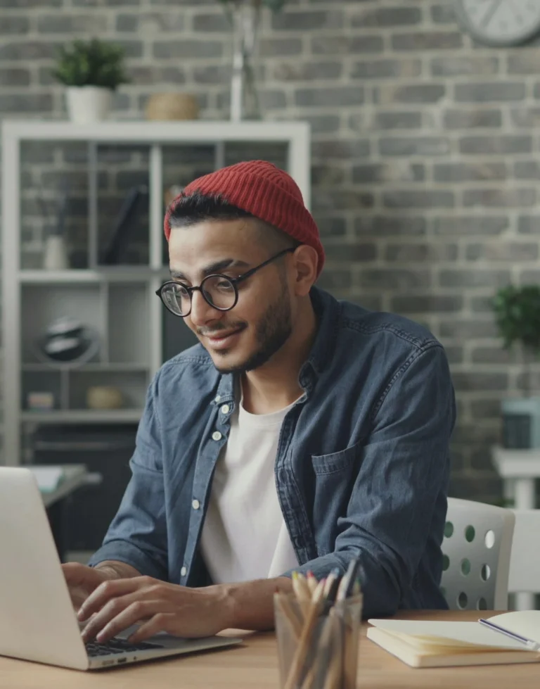 Photo d'un homme à lunette et bonnet rouge qui travaille sur un ordinateur en souriant